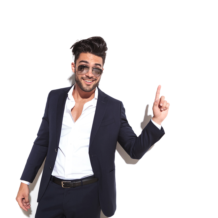 Cool business man wearing sunglasses smiling and pointing up, having a good idea, against a white background