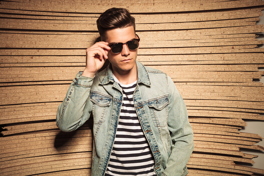 cool young casual man taking off his sunglasses and looks to a his on wooden studio background