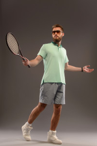 Practicing tennis. Handsome young man holding tennis racket and playing tennis while standing isolated on grey background